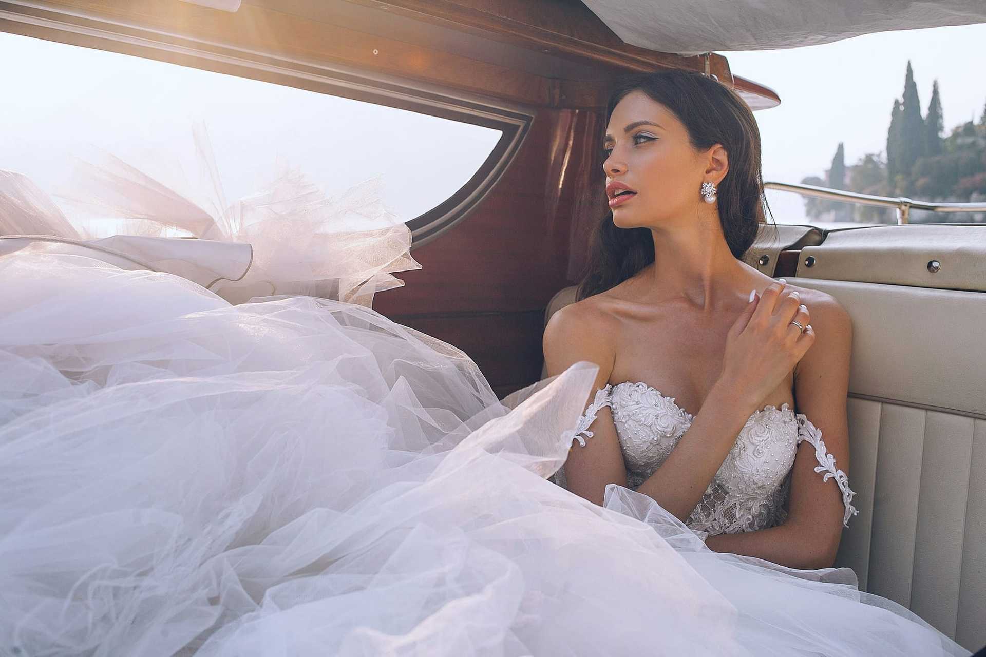 Bride in a white gown sitting on a boat, looking thoughtfully into the distance.