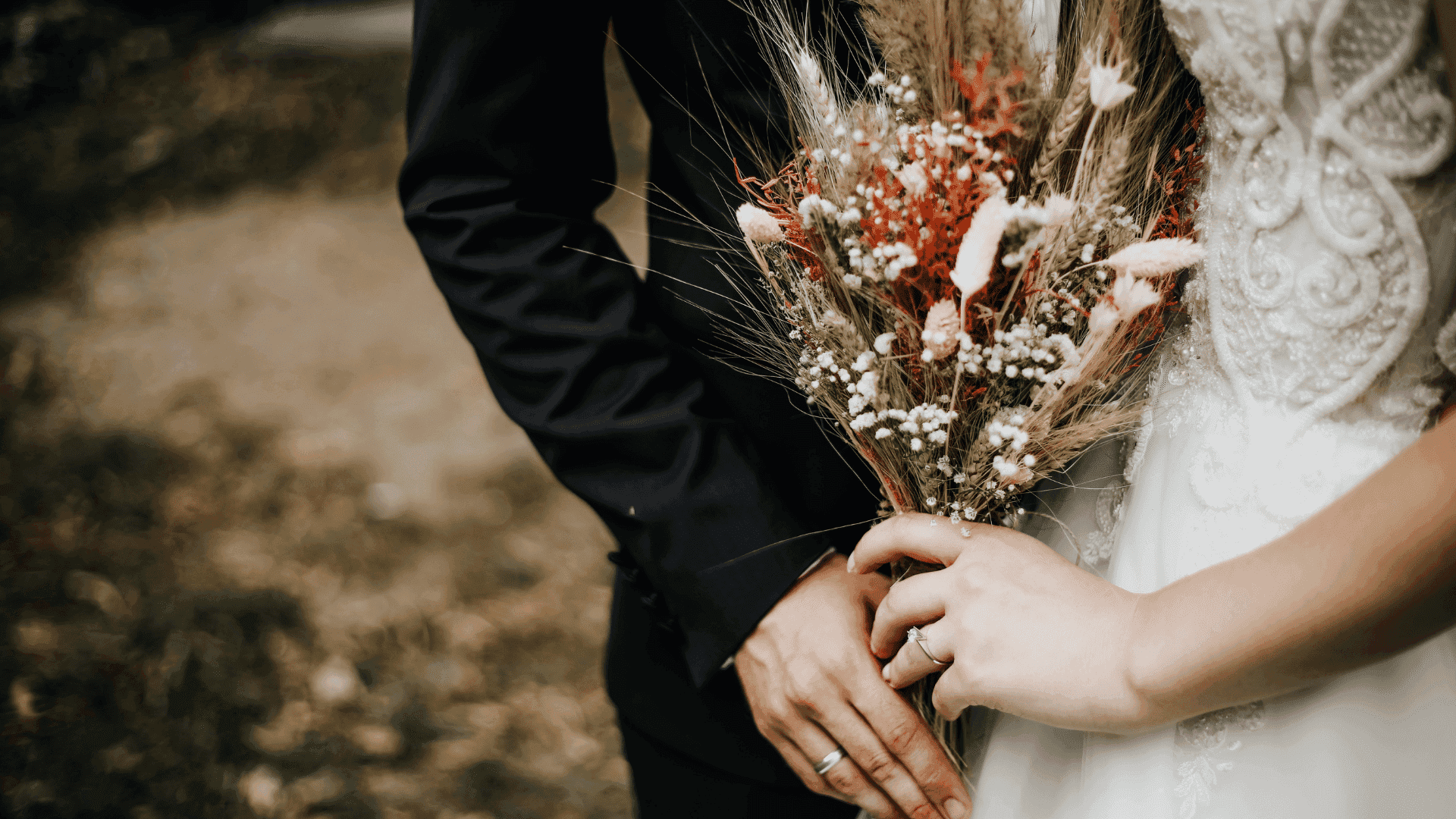 Bride and groom holding a rustic bouquet with dried flowers.