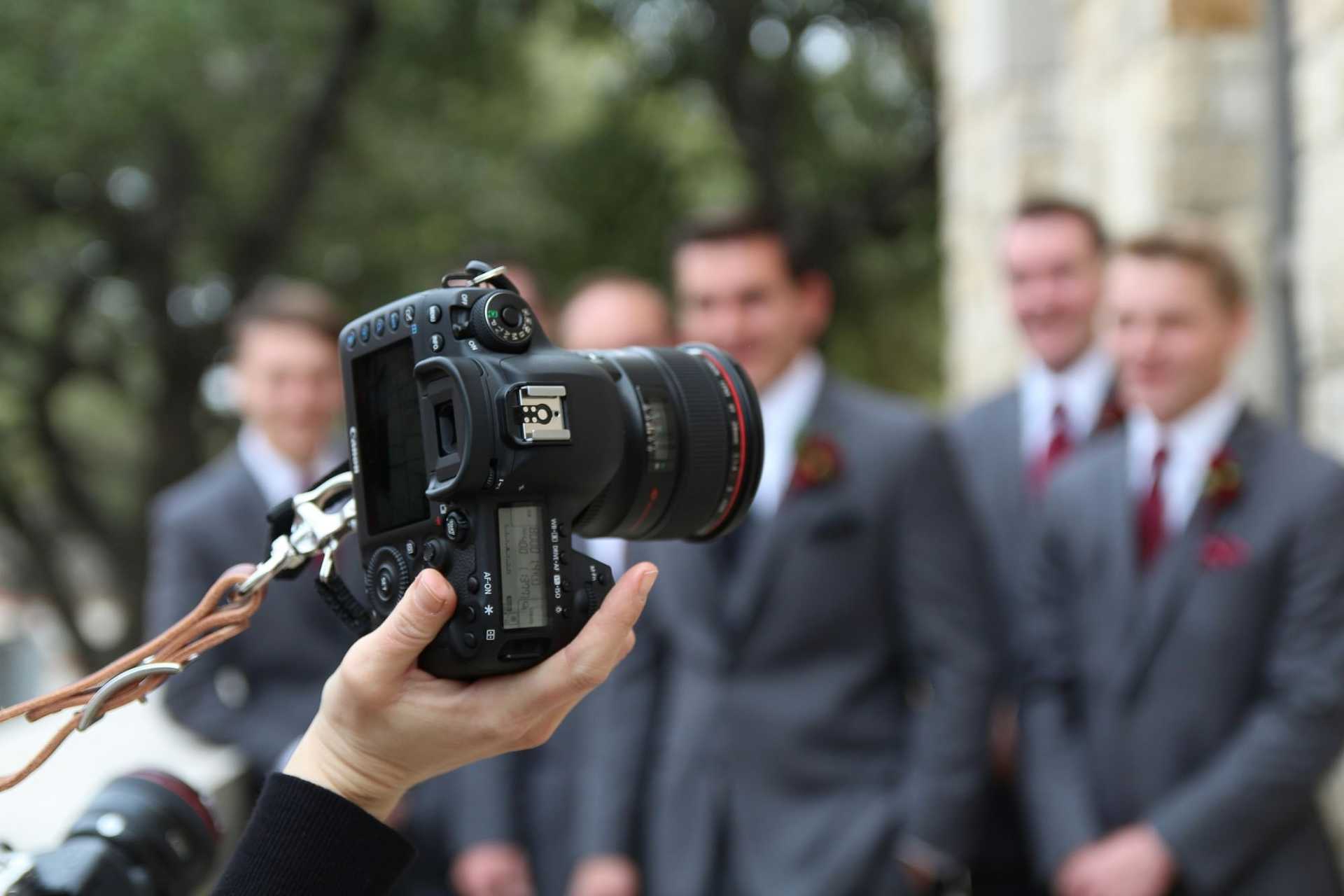 Camera focusing on a group of groomsmen in gray suits outdoors.