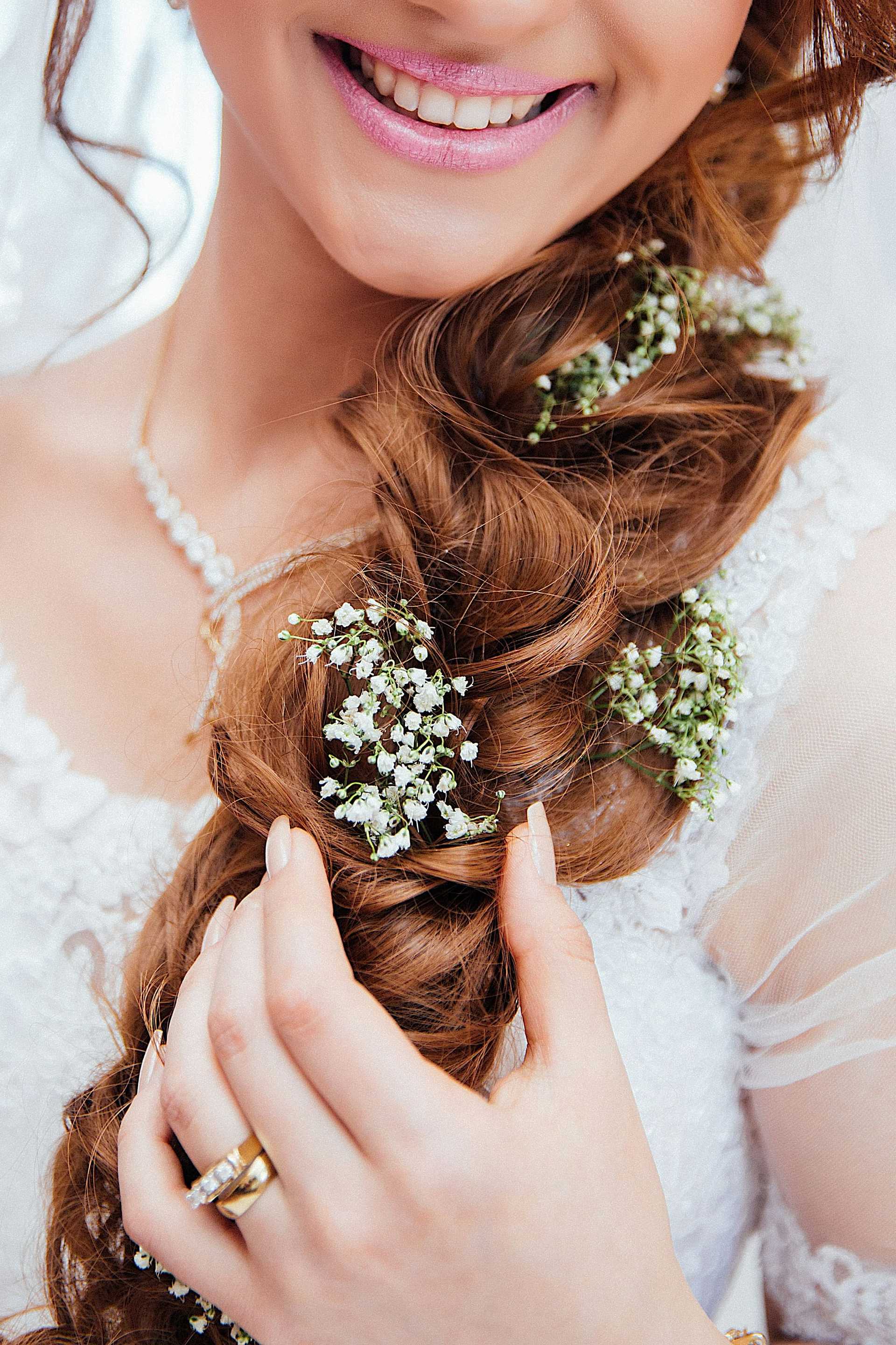 Bride's braided hair with flowers, wearing lace dress and pearl necklace.