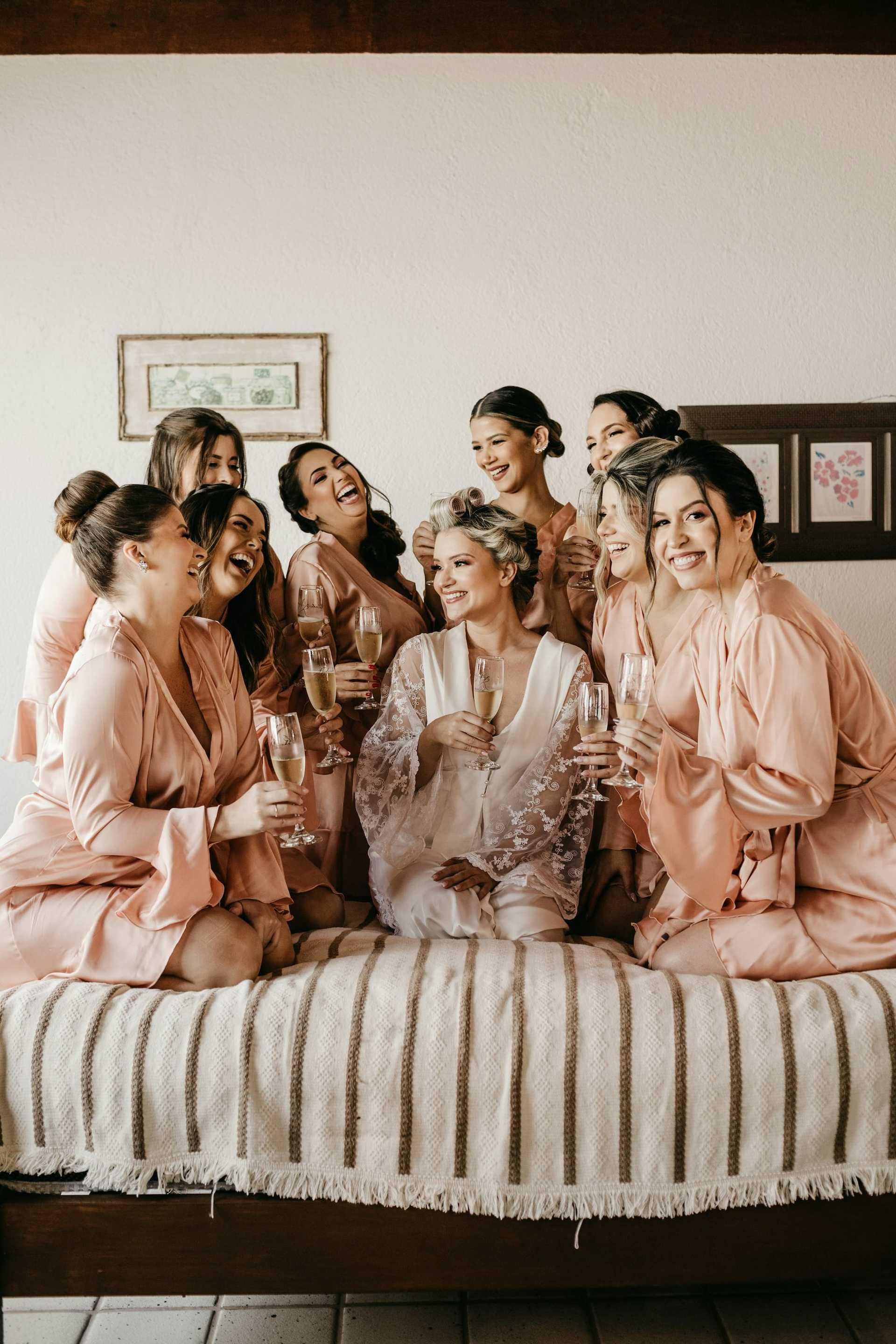 Bridal party in robes enjoying champagne and laughter on a bed.