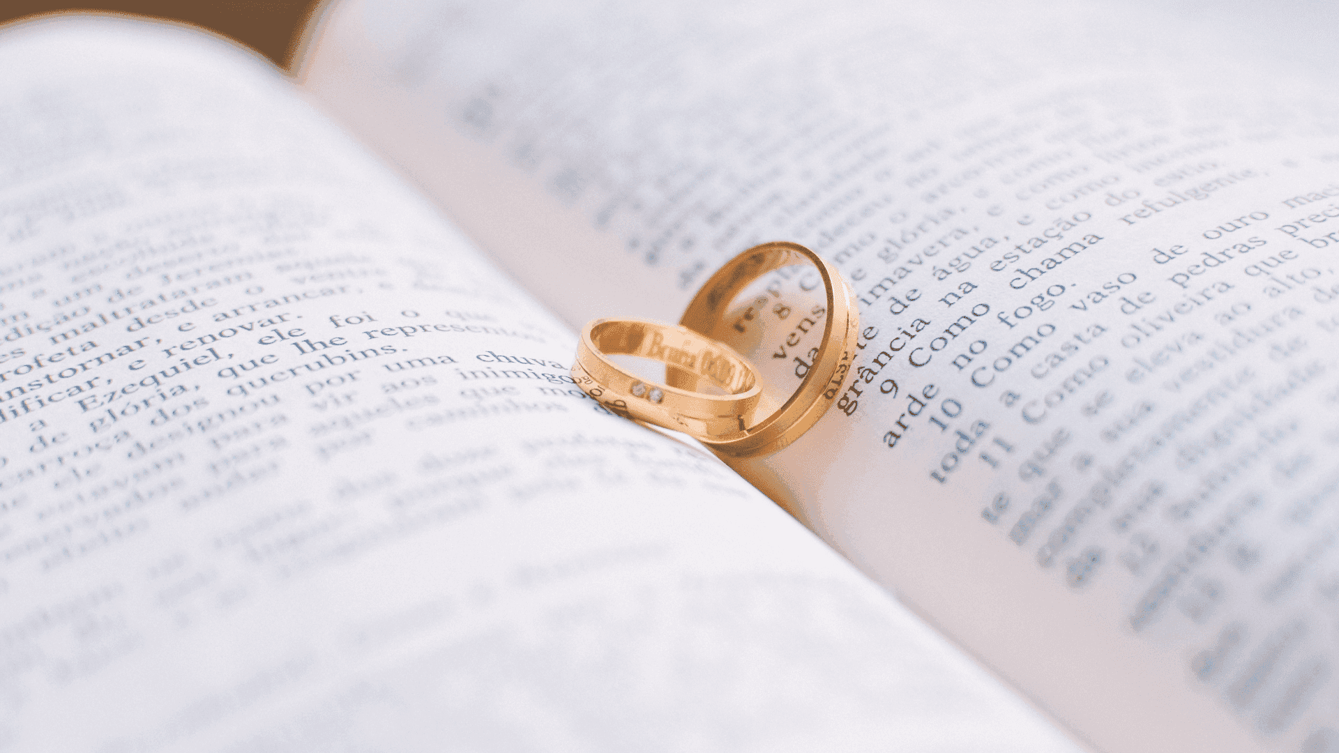 Two gold wedding rings resting on an open book's pages, symbolizing love and commitment.